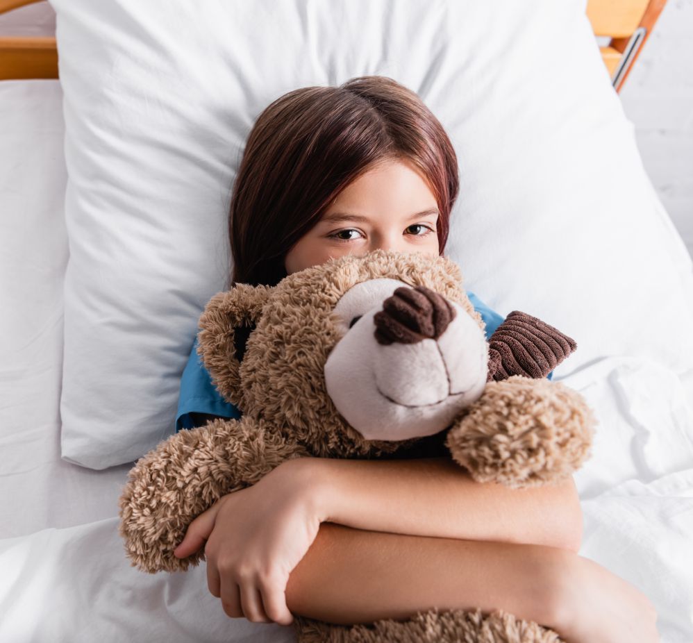 girl in bed holding a teddy bear